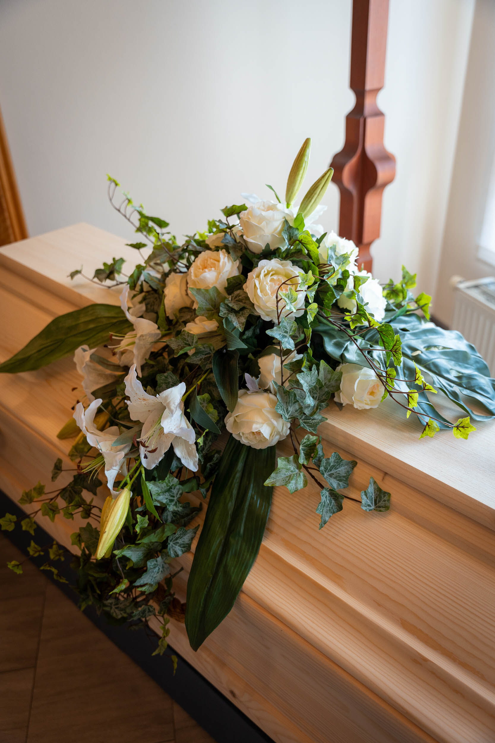 Gesteck aus weißen Rosen und anderen hellen Blumen auf einem Sarg im Bestattungsinstitut Gann